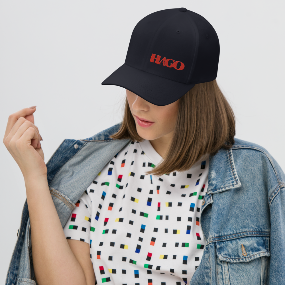 Person wearing a black cap with 'HAGO' logo, colorful patterned shirt, and denim jacket on a white background