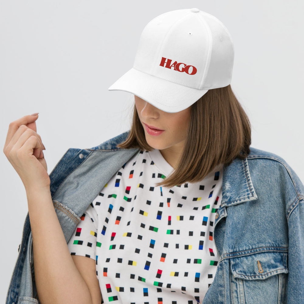 Person wearing a white cap with 'HAGO' logo, colorful patterned shirt, and denim jacket on a light gray background